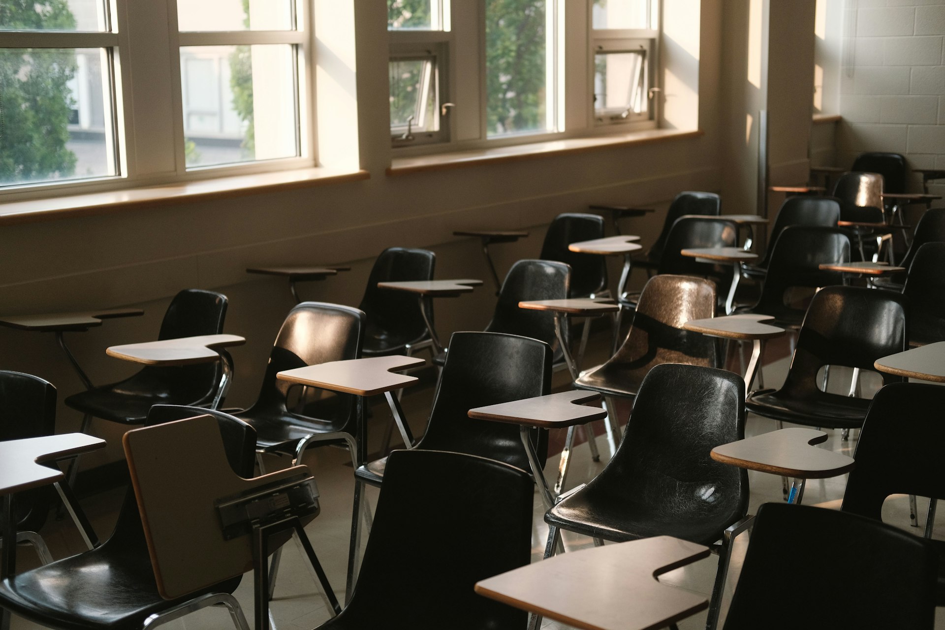 A classroom set up with rows of desks and chairs beside large windows