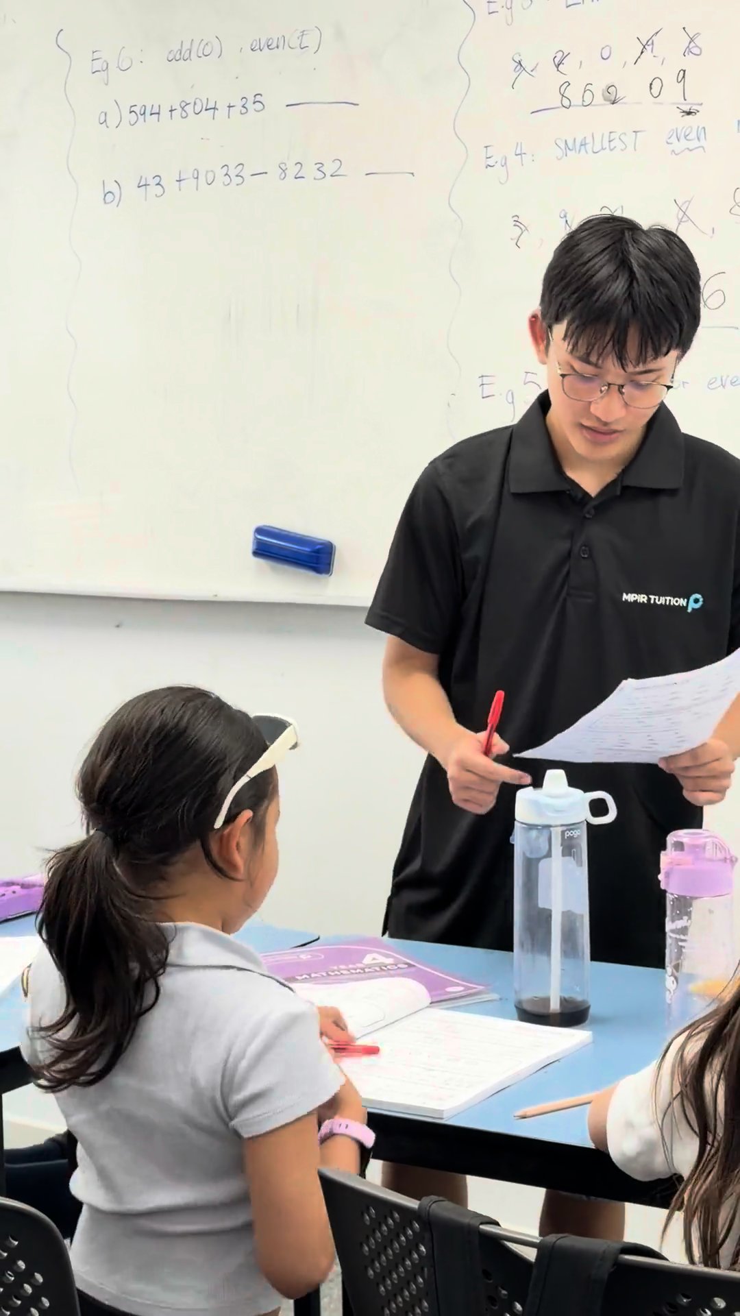 A Signal tutor standing at the whiteboard, checking a young student's work mid-lesson